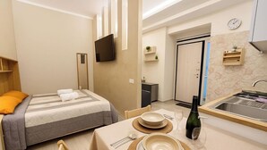 Habitació d'hotel senzilla amb llit, taula de nit i petita cuina.
