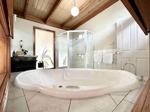 Ein Badezimmer mit einer großzügigen Badewanne, einer Duschkabine aus Glas und einer Holzbalkendecke.