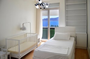 Un dormitorio con una cuna, una cama, un escritorio y un ventanal con vistas al exterior.