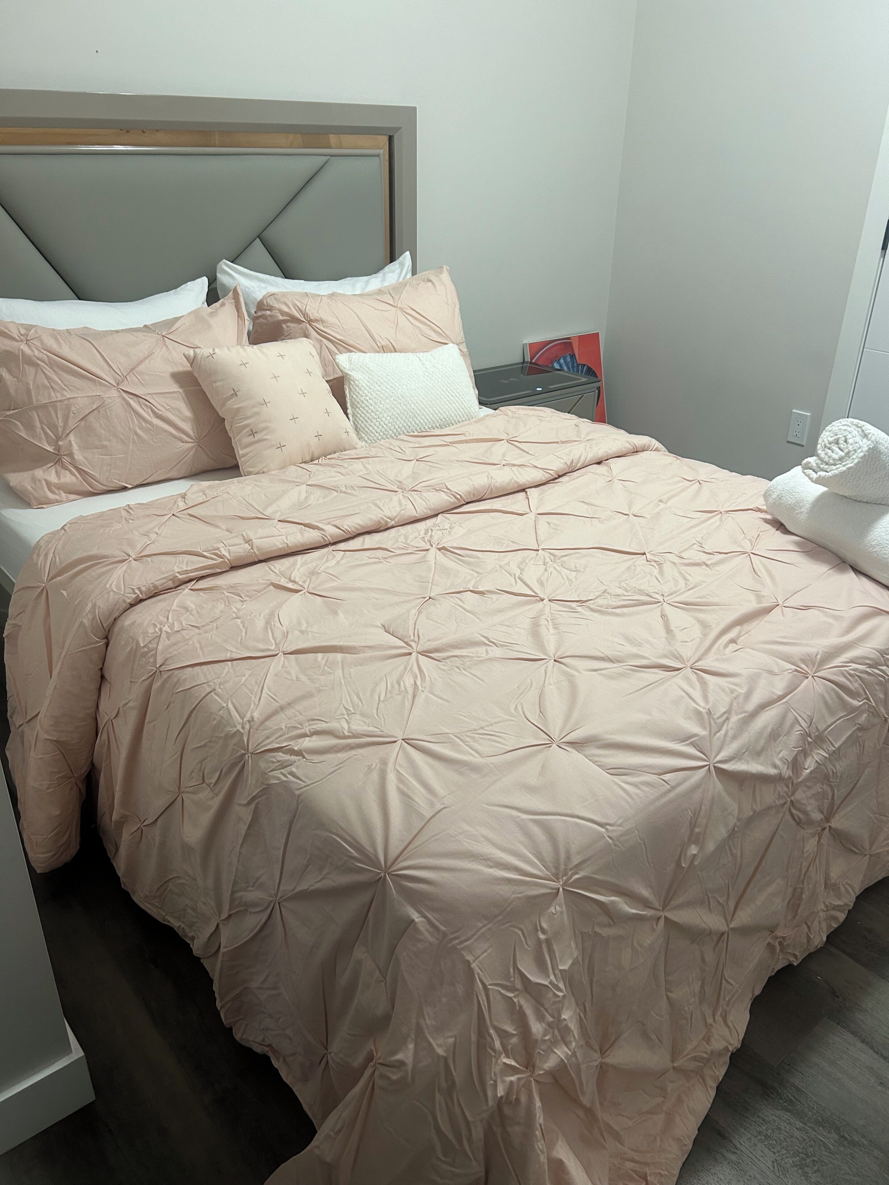 Un lit bien fait, avec une couette et des oreillers de couleur beige, une tête de lit en bois et un mur blanc.