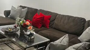 Un soggiorno con un divano marrone, un tavolino da caffè in vetro e un vaso con fiori.