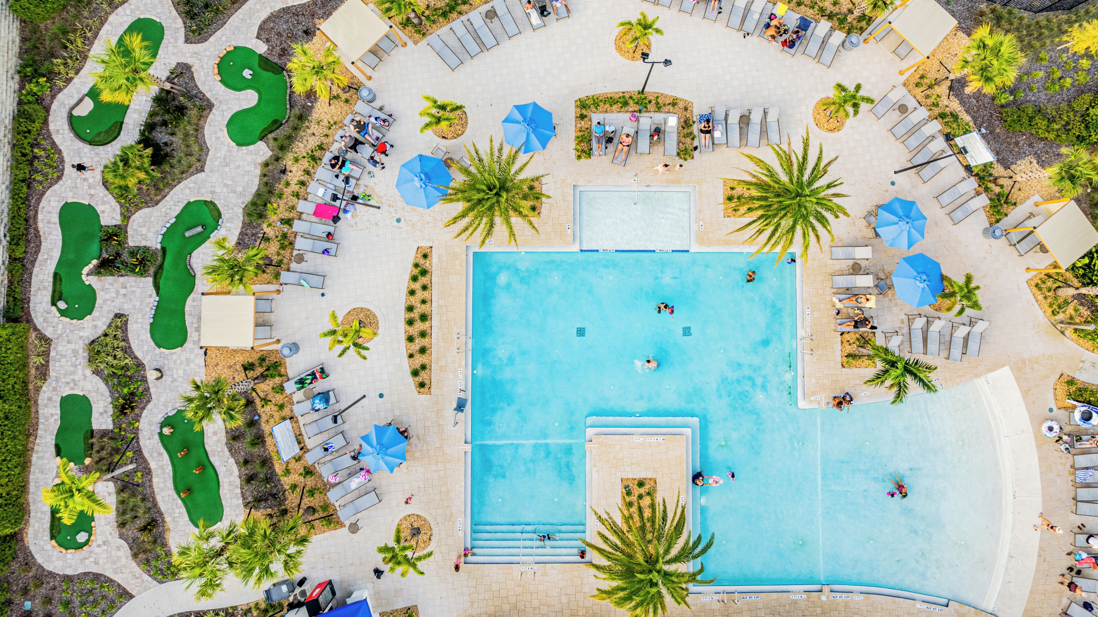 An aerial view of a resort with a central swimming pool, multiple lounge areas, and landscaped gardens.