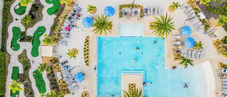 An aerial view of a resort with a central swimming pool, multiple lounge areas, and landscaped gardens.