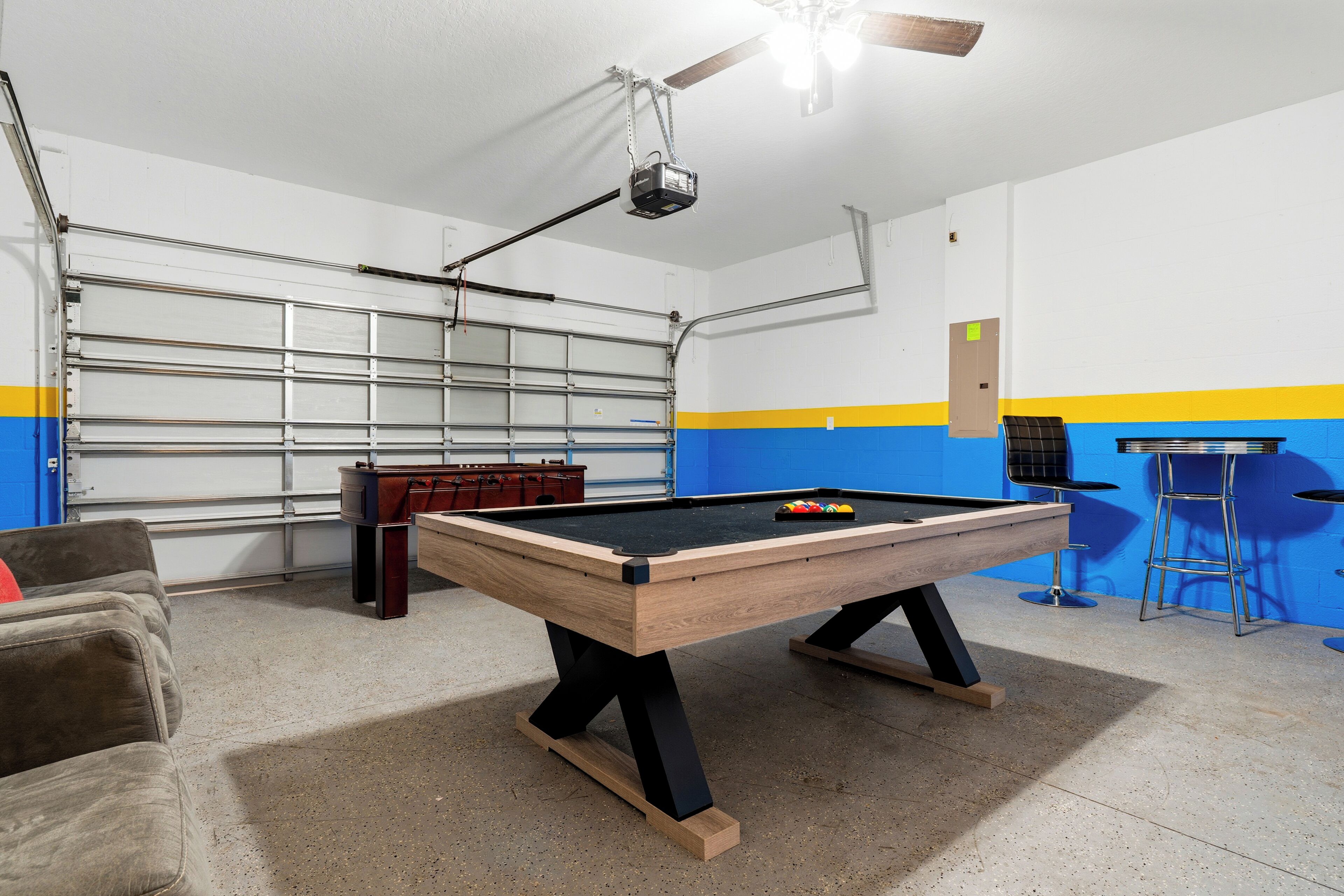 A pool table in a room with a ceiling fan, a garage door, and a blue and yellow wall.