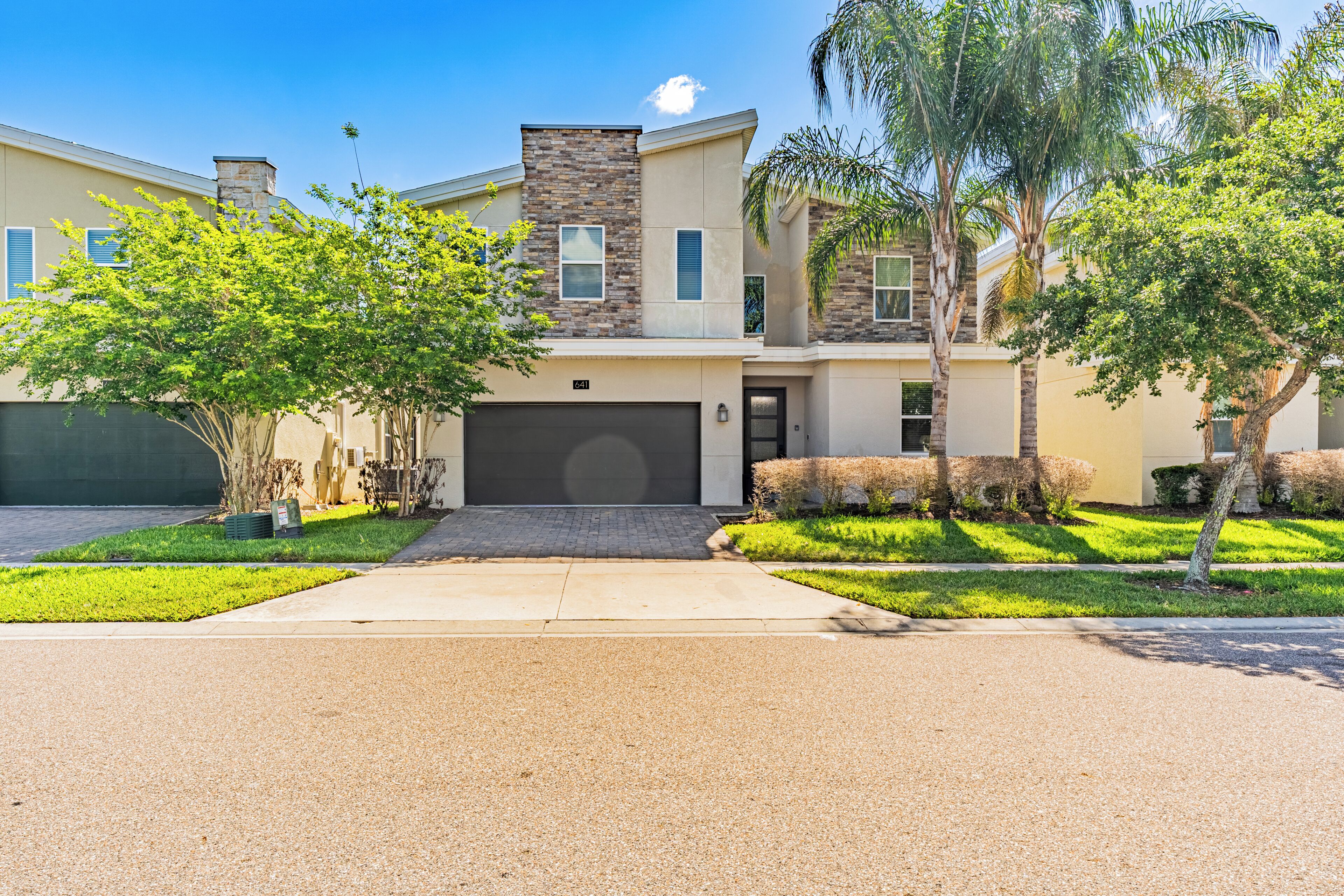 A modern two-story house with a garage, a well-maintained lawn, and mature trees.