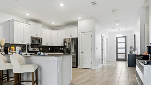 A modern kitchen with white cabinetry, a central island, bar stools, and a stainless steel refrigerator. - Nine Bedroom Vacation Home ChampionsGate (Davenport)