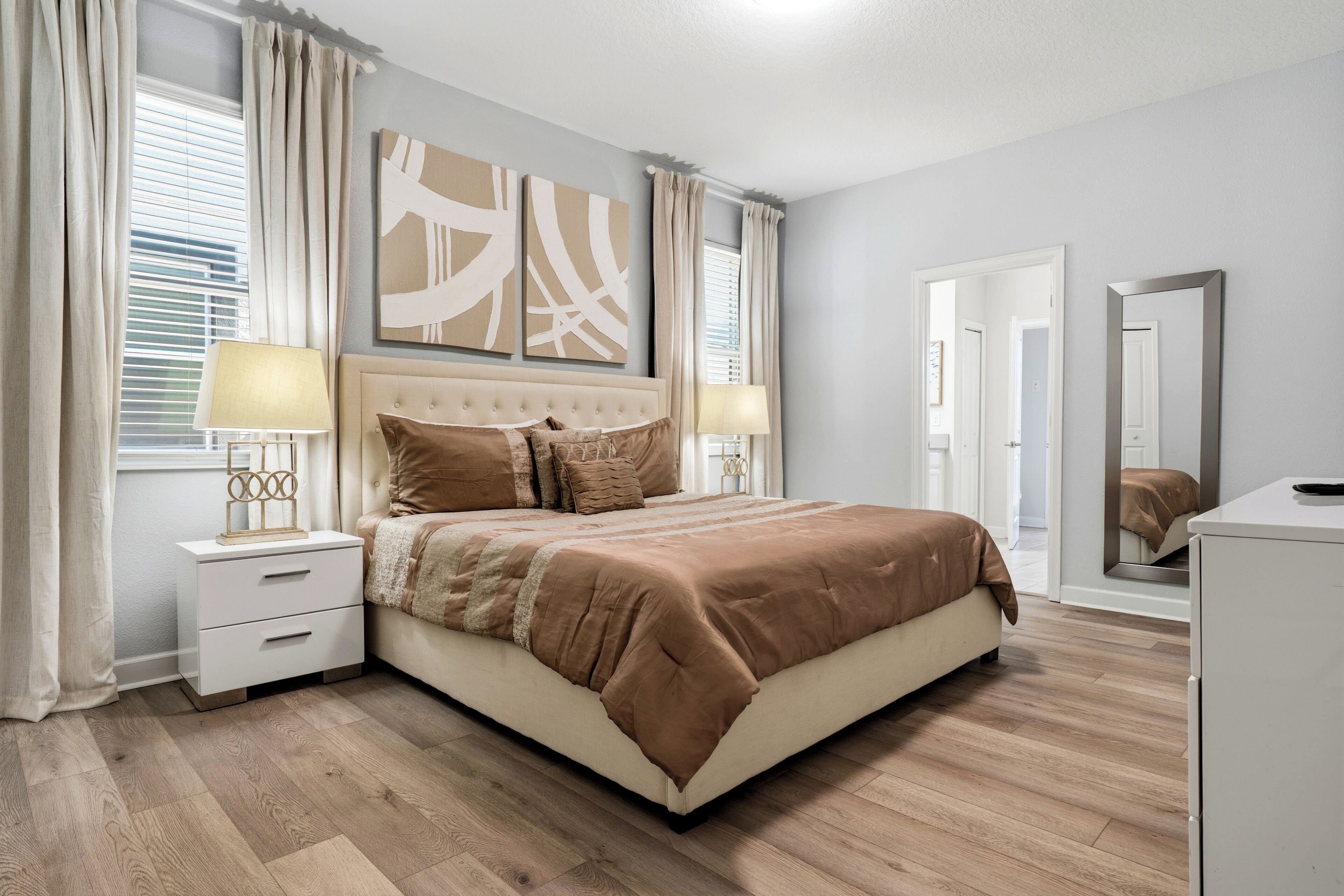 A bedroom with a bed, nightstands, a dresser, a mirror, and artwork on the wall.