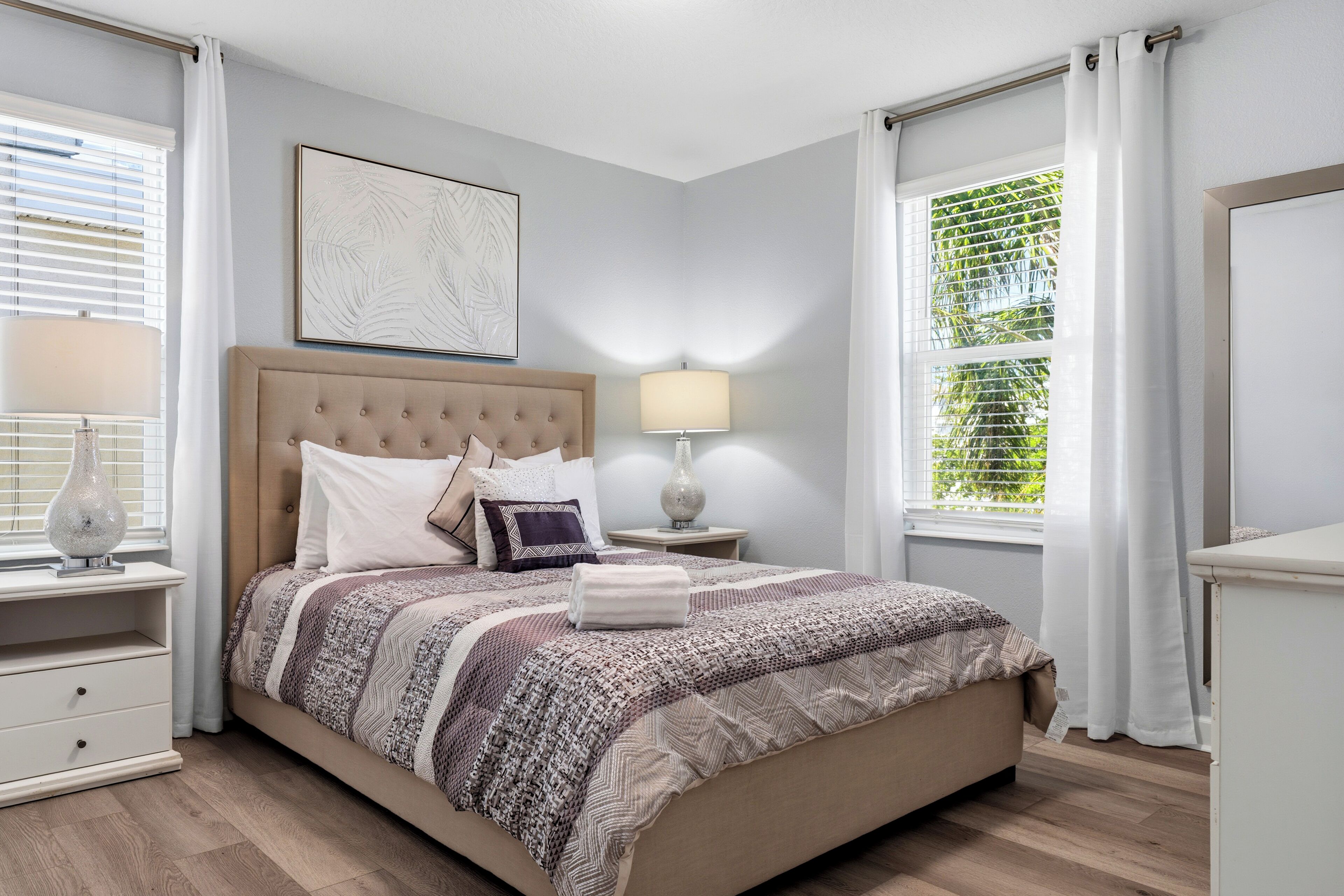 A bedroom with a bed, bedside tables, a lamp, a window with curtains, and a wall art piece.