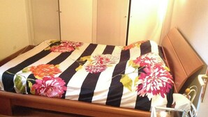 A bed with a floral-patterned bedspread, a wooden headboard, and a bedside table with a lamp. - Independent apartment for rent in a villa on the 1st floor in Saint Jean de Luz. (Saint-Jean-de-Luz)