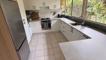 Una cocina moderna con armarios blancos, un refrigerador de acero inoxidable y una ventana con vista a zonas verdes.