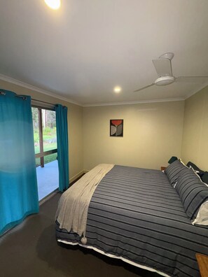 A bedroom with a bed, a ceiling fan, a window with curtains, and a painting on the wall.