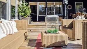 A wooden deck with wicker furniture, a glass enclosure with plants, and a clear view of the house.