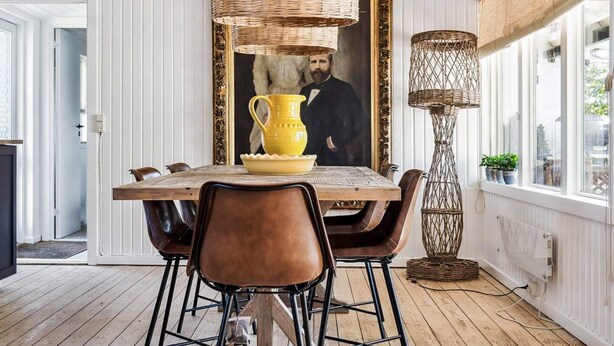 A dining area with a wooden table, brown leather chairs, a yellow pitcher, and a framed portrait.