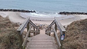 A wooden staircase leading to a beach with a rocky shoreline and a warning sign.