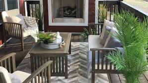 A covered porch with a fireplace, wooden furniture, and potted plants.