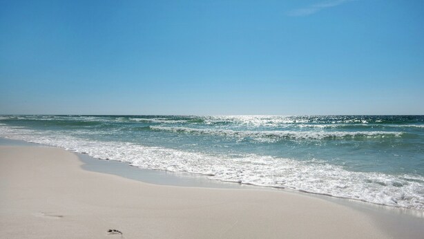 Une plage avec un ciel dégagé et des vagues sur l’océan.