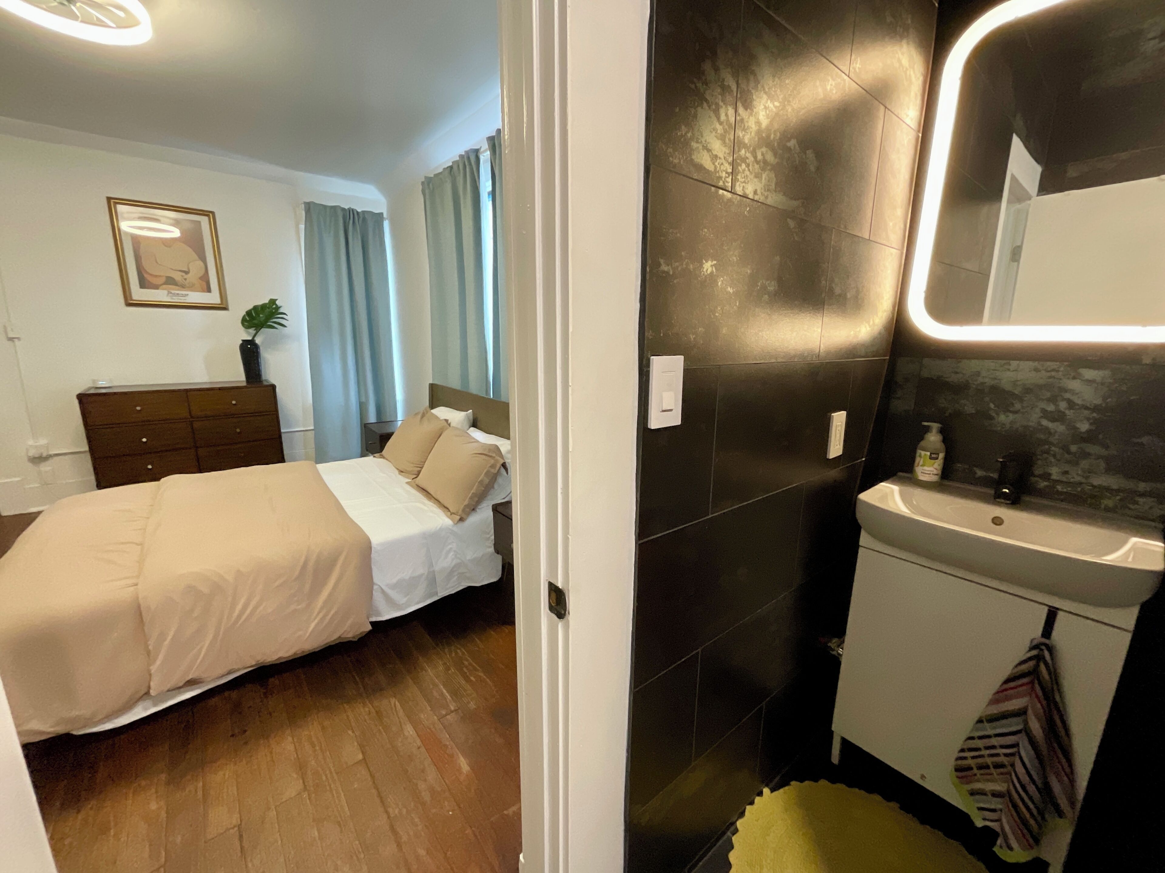 Un dormitorio con cama, cómoda, mesita de noche, un cuadro enmarcado y ventana con cortinas.