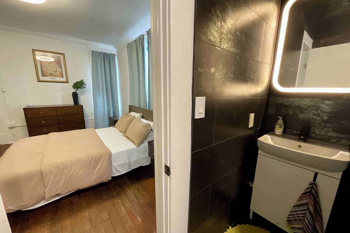 A bedroom with a bed, a dresser, a nightstand, a framed picture, and a window with curtains.
