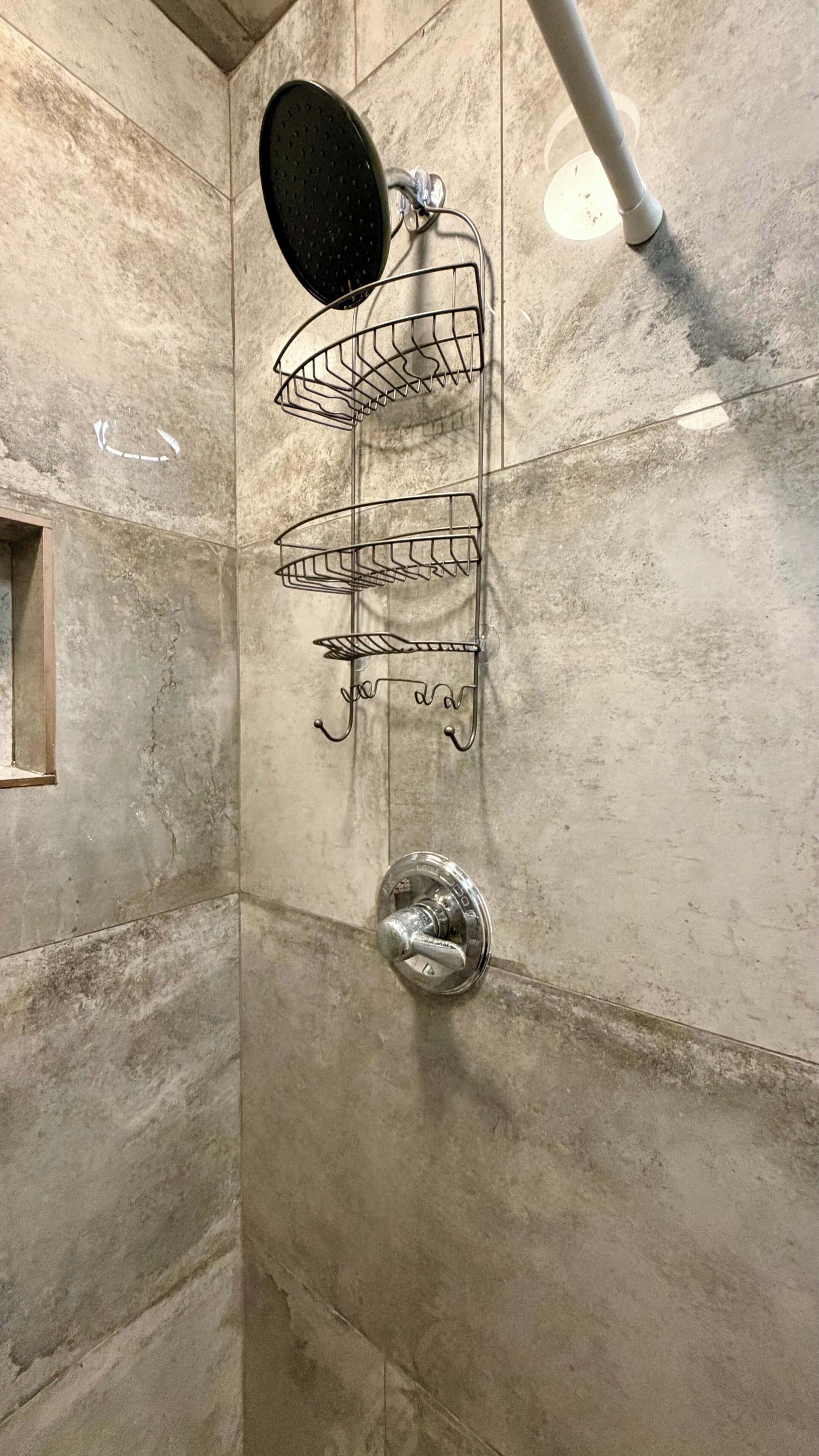A shower with a black circular head, a metal rack, and a silver faucet.