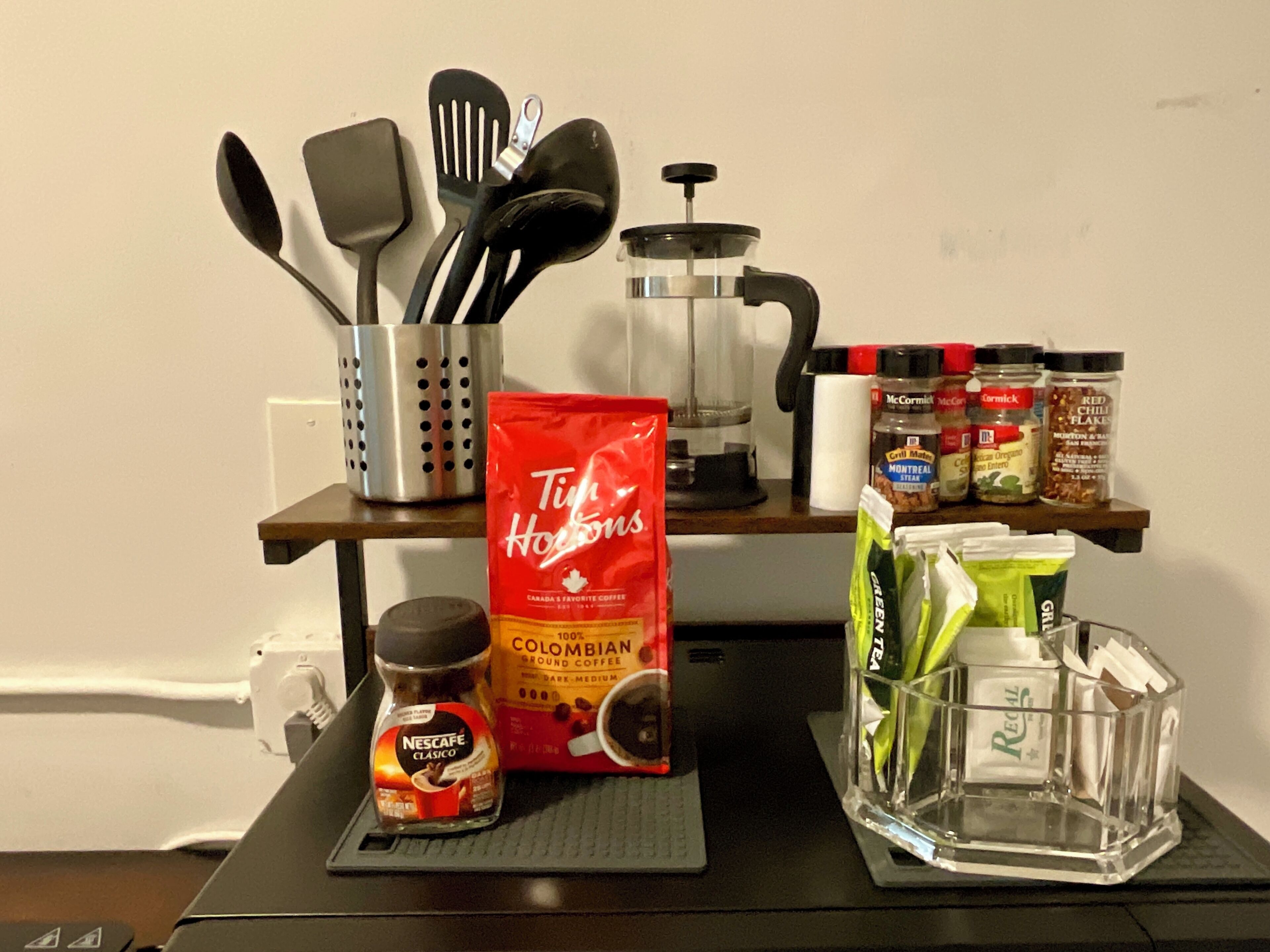 A kitchen counter with a coffee maker, a bag of Tim Hortons coffee, a jar of Nescafe, and various spices.