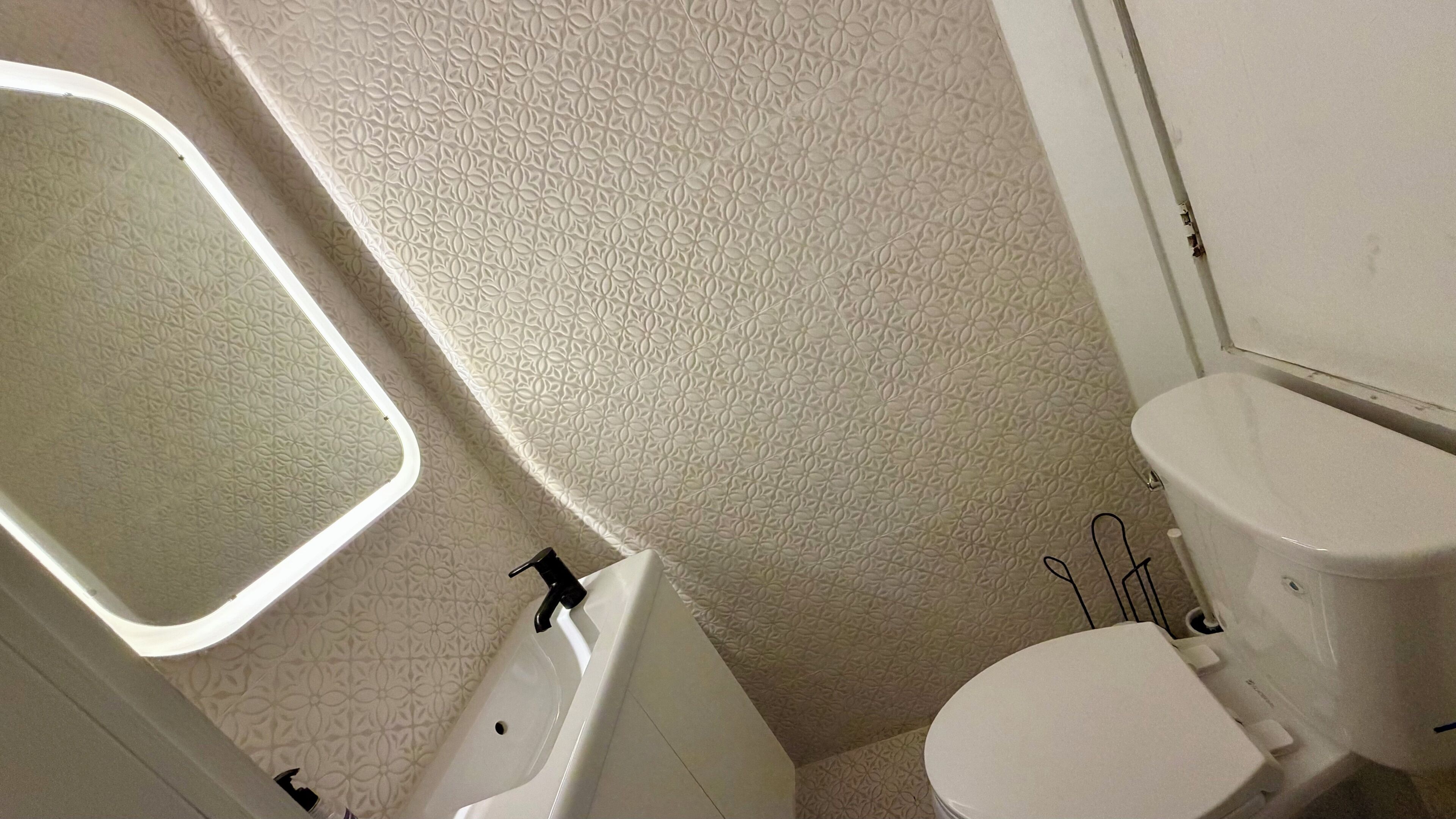 Une salle de bain avec des toilettes blanches, un lavabo et un miroir.