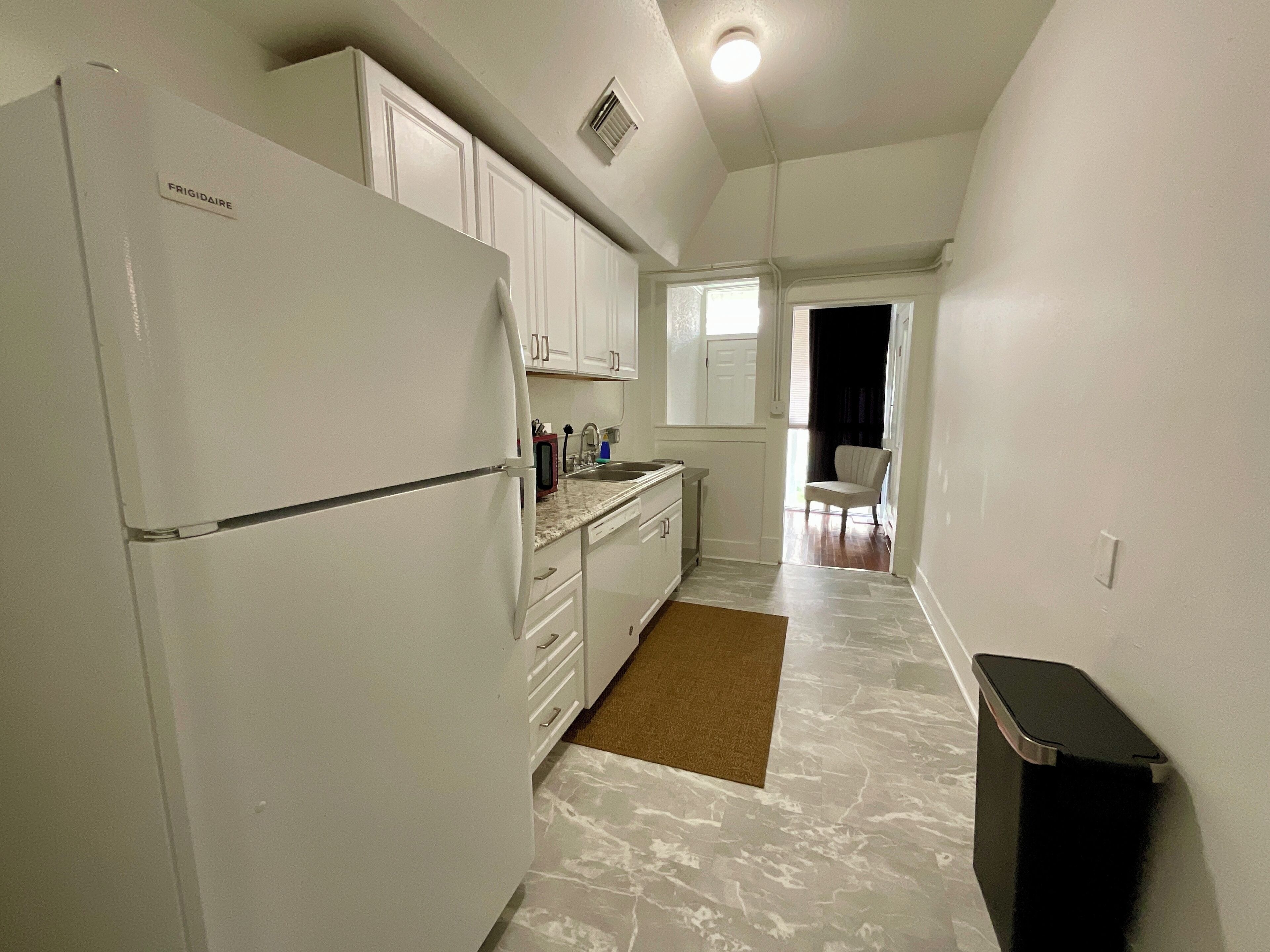 Cocina compacta con armarios blancos, un refrigerador, un microondas y un lavamanos.