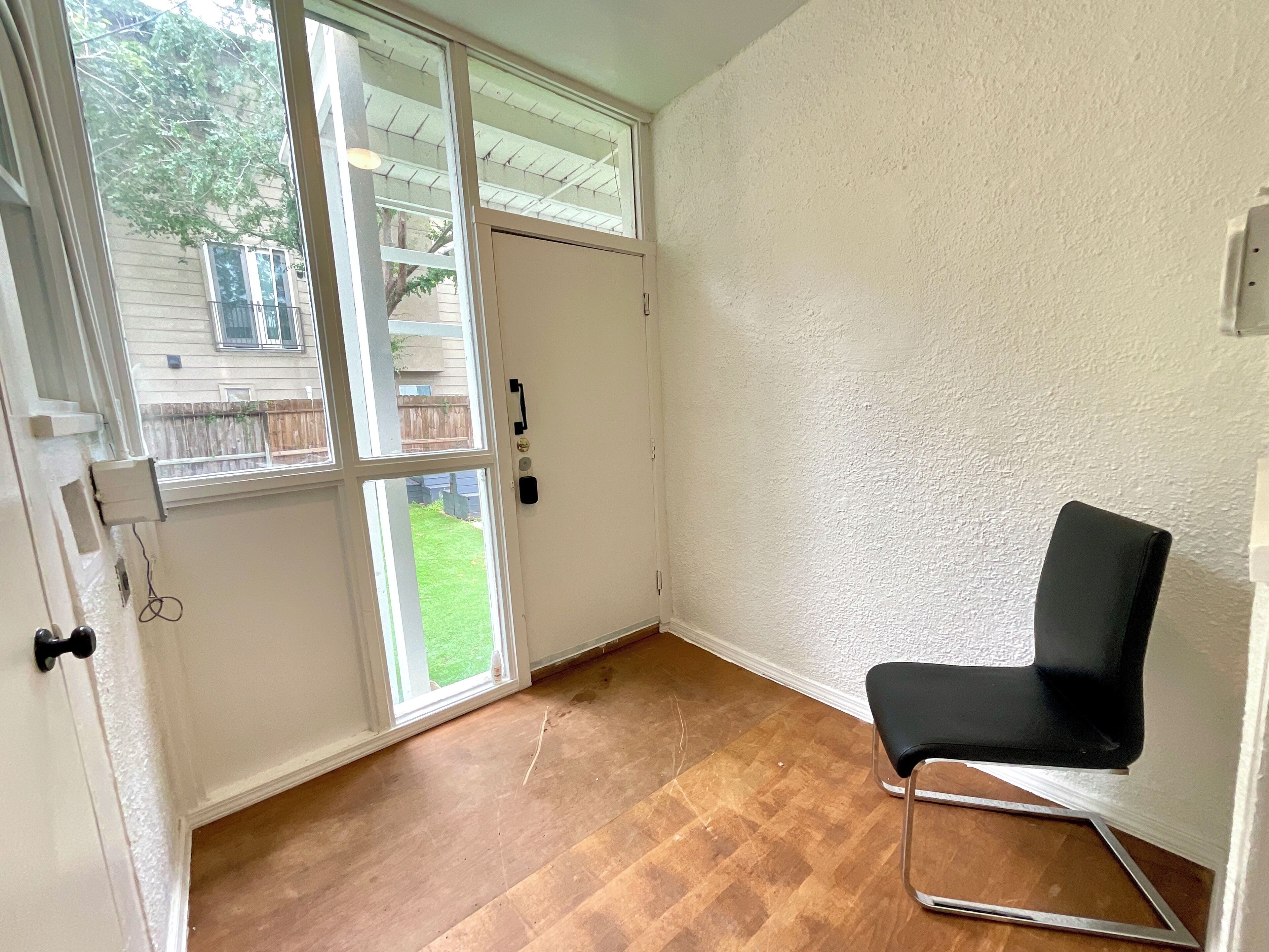 A room with a sliding glass door leading to a backyard, a black chair, and a textured white wall.