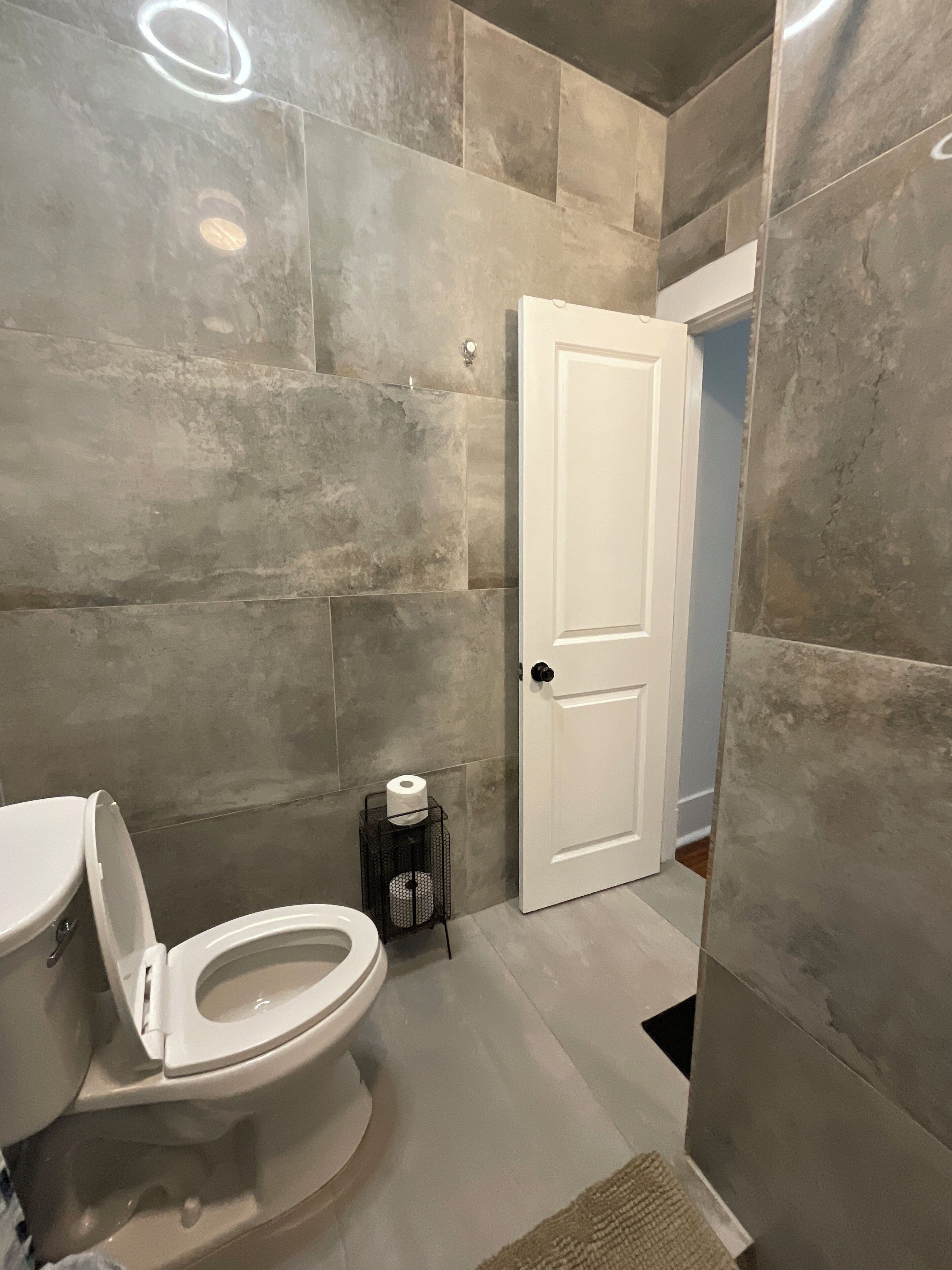 A bathroom with a toilet, a door, and a small trash bin.