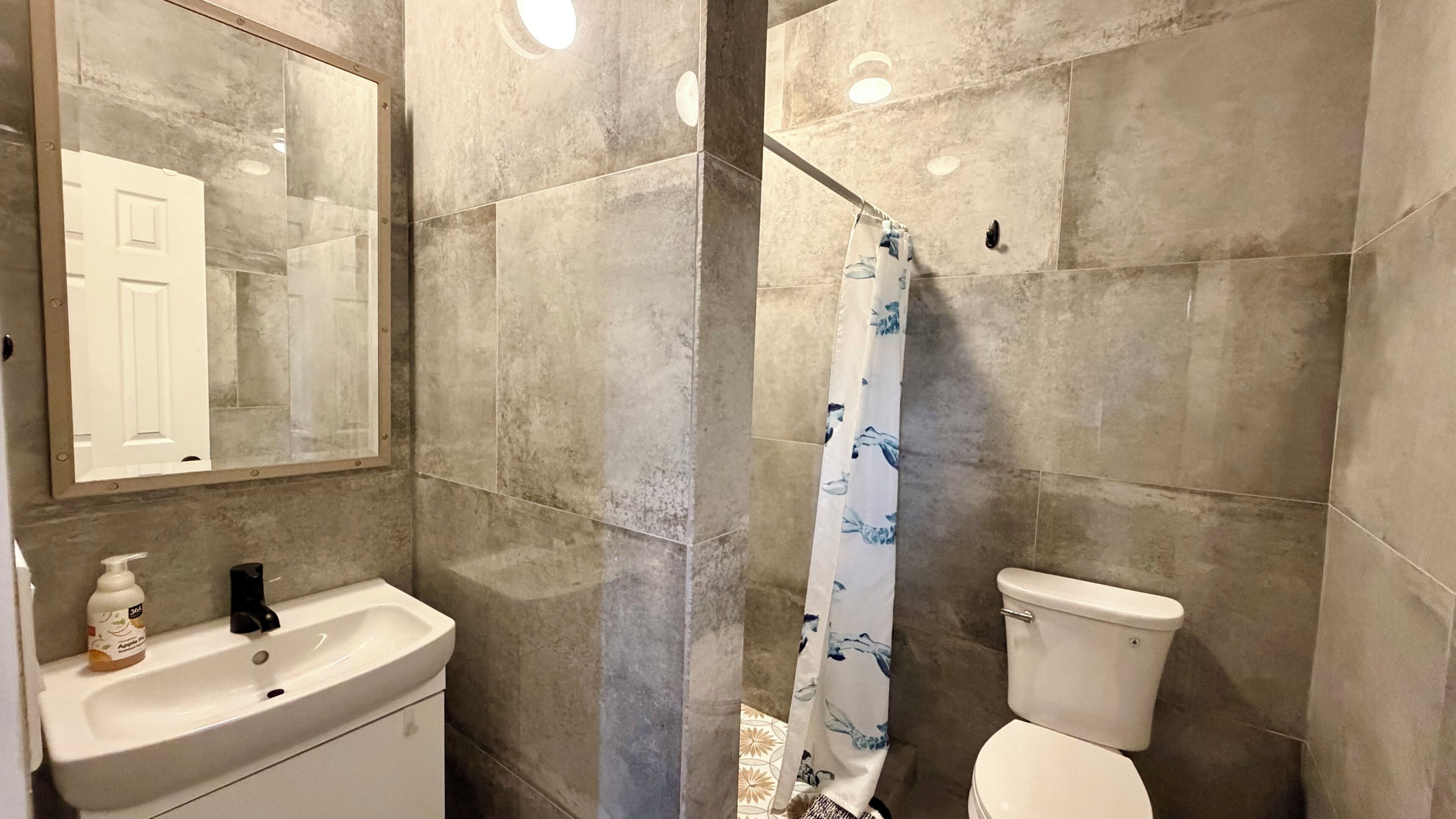 A bathroom with a sink, mirror, toilet, and shower curtain.