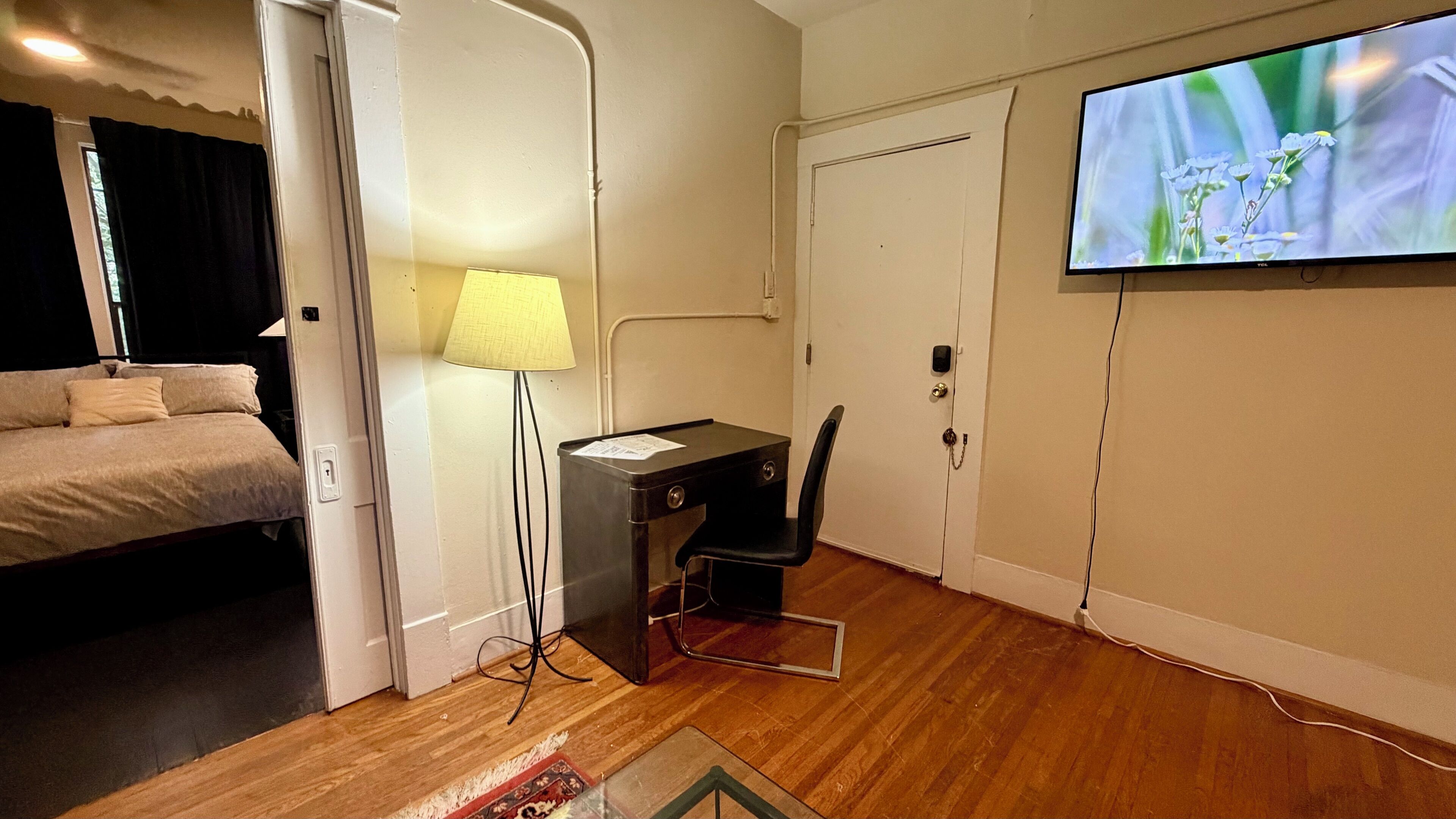 A hotel room with a bed, desk, chair, TV, and a door.