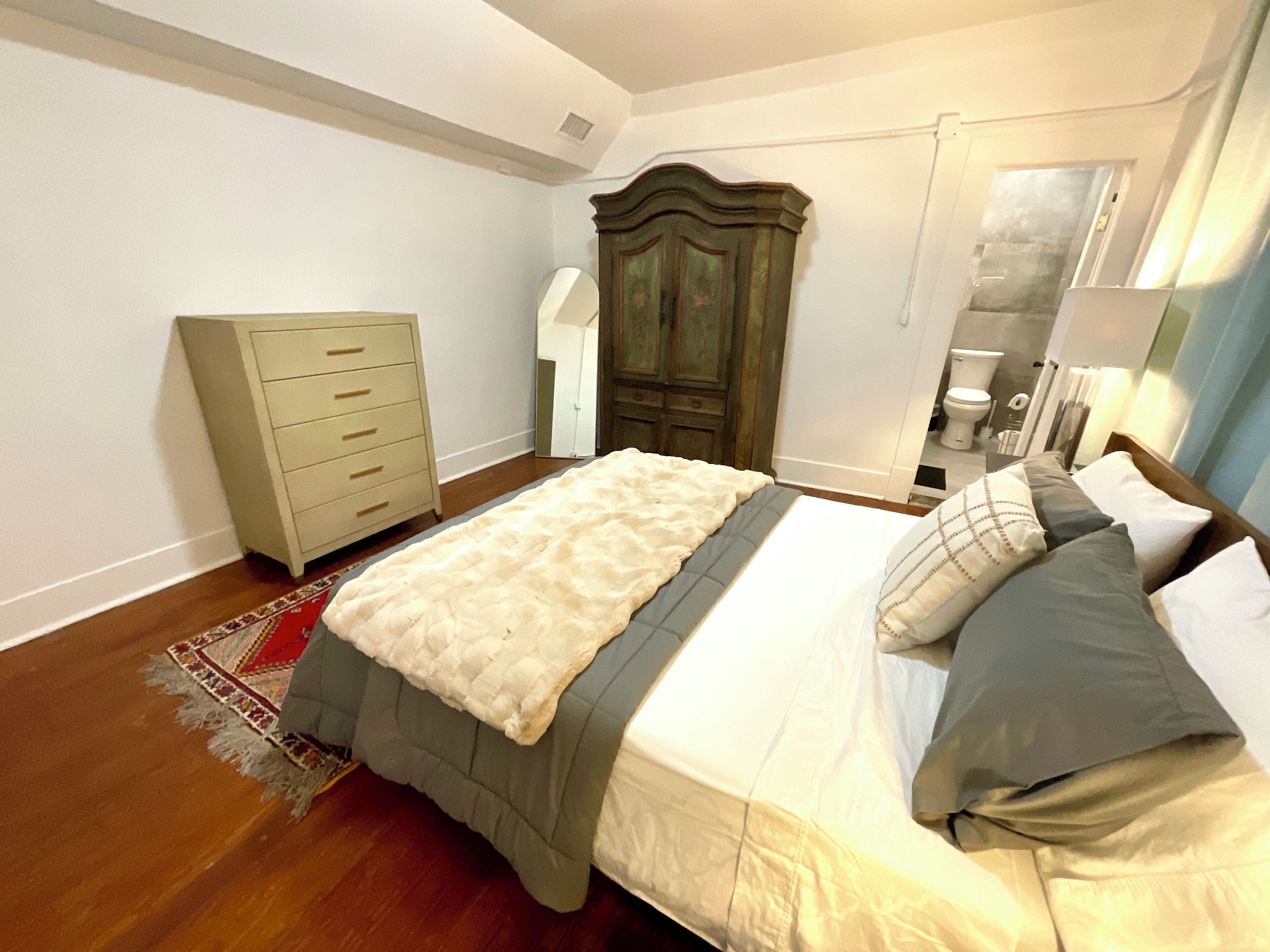 A bedroom with a bed, a dresser, a wardrobe, and a bathroom visible through an open door.