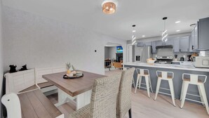 Eine moderne Küche mit grauen Schränken, einer zentralen Kochinsel inklusive Barhocker und einem Essbereich mit einem Holztisch und Korbstühlen.