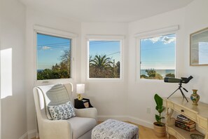 Una habitación con vista al océano, un telescopio y una estantería.