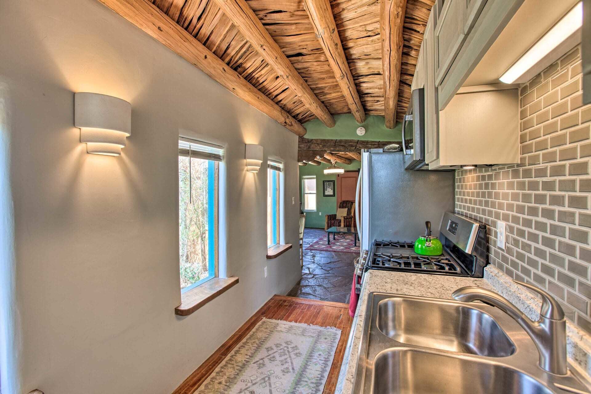 A kitchen with a stone floor, wooden ceiling beams, and a brick backsplash.