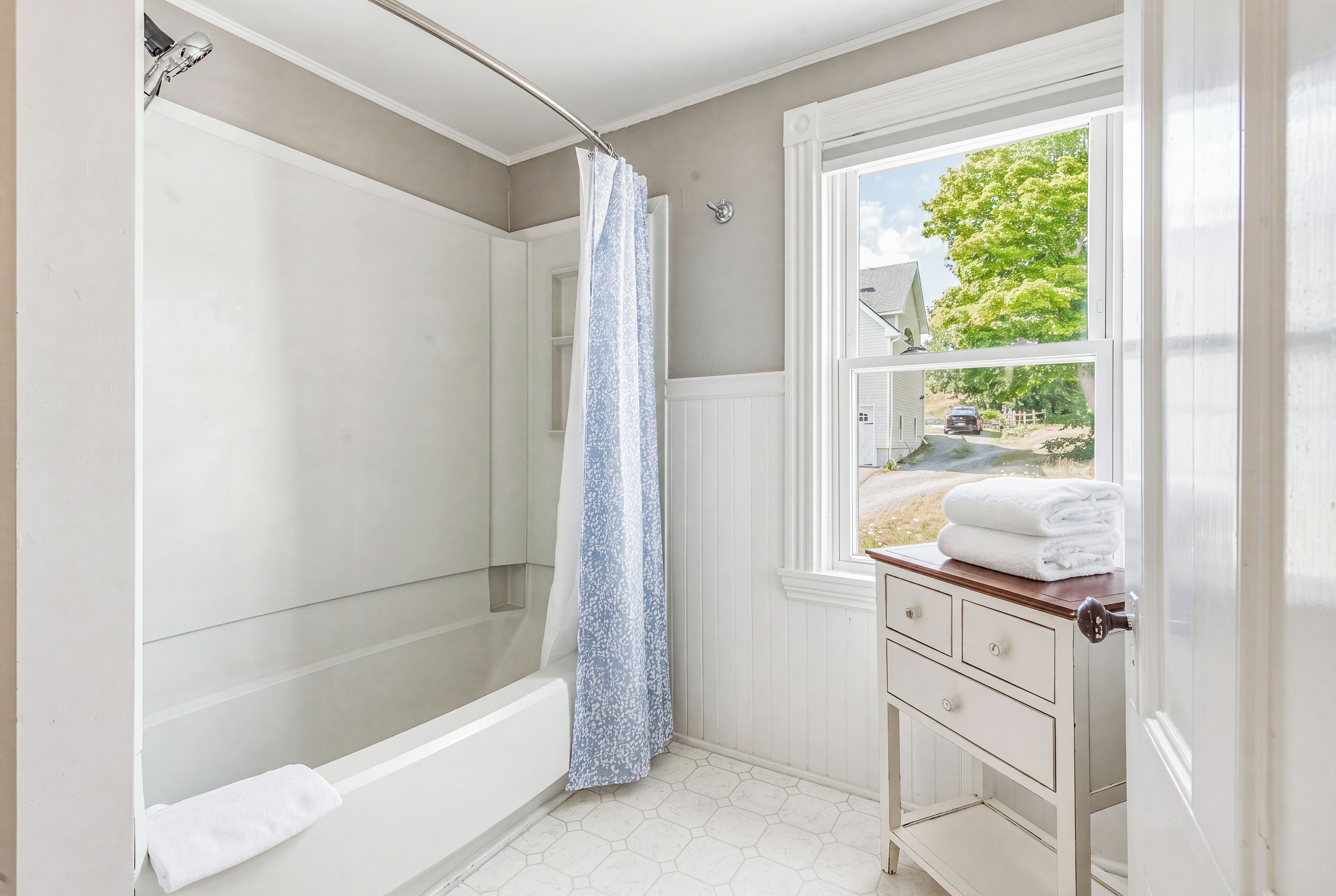 A bathroom with a bathtub, a shower curtain, a window with a view of the outside, and a vanity with a towel.