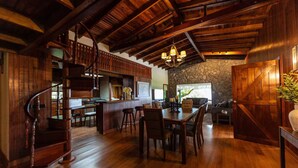 Un interno rustico con una scala in legno, un muro in pietra, una zona pranzo e un bar.