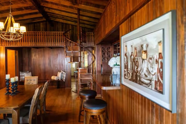 A wooden interior with a dining area, a staircase, and a framed artwork on the wall.