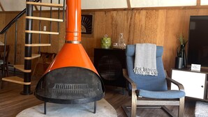 A modern living room with a wooden staircase, a round orange heater, a blue armchair, and a flat-screen TV.