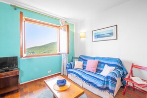 Een kamer met een groot raam, een bank, een televisie, een tafel en een stoel.