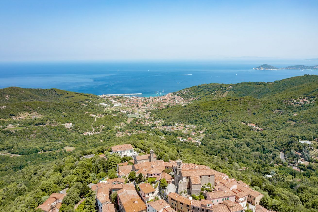 Un villaggio costiero con edifici a tetto di tegole rosse, una chiesa centrale e vista sul mare.