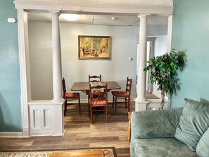 Een eetgedeelte met een tafel, stoelen, een schilderij aan de muur en een plant in de hoek.