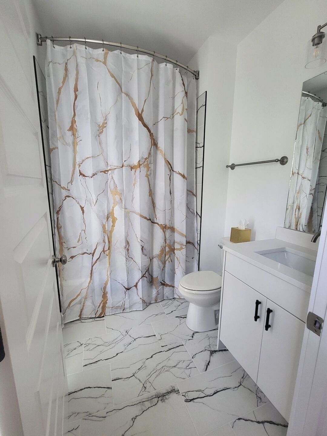 A bathroom with a shower curtain, toilet, sink, and cabinets.