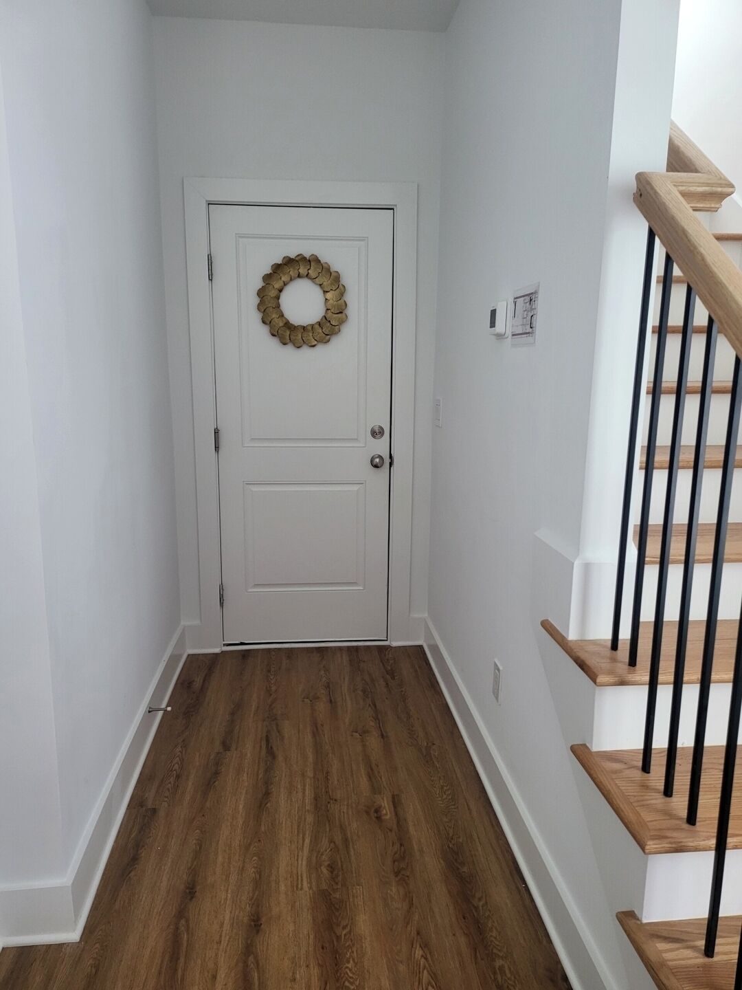 A hallway with a white door, a wooden floor, and a wooden staircase with black railings.