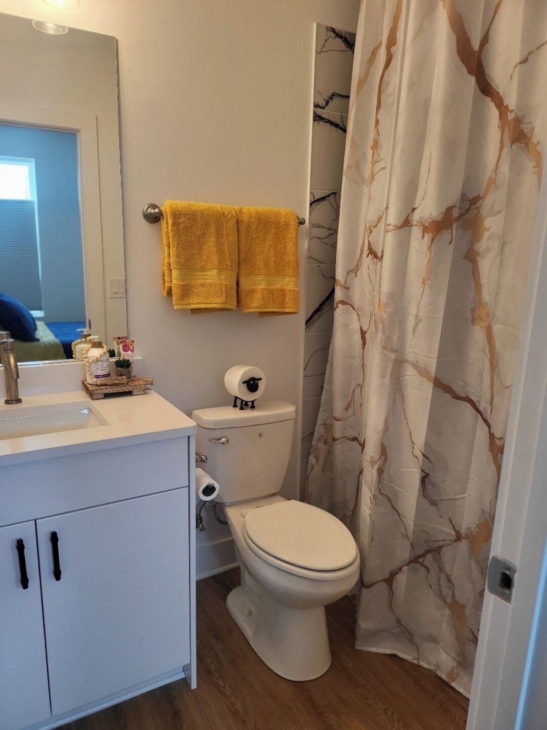 Un baño con inodoro, lavamanos y espejo. Hay dos toallas amarillas colgadas en la pared.