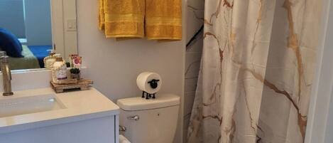 Un baño con inodoro, lavamanos y espejo. Hay dos toallas amarillas colgadas en la pared.