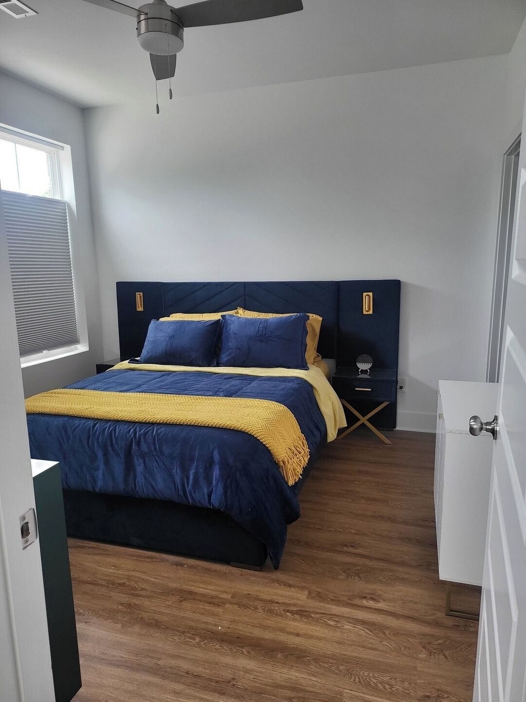 Un dormitorio con una cama, ventilador de techo, mesita de noche y cómoda.