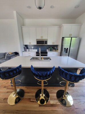 A modern kitchen with a central island, stainless steel appliances, and bar stools.