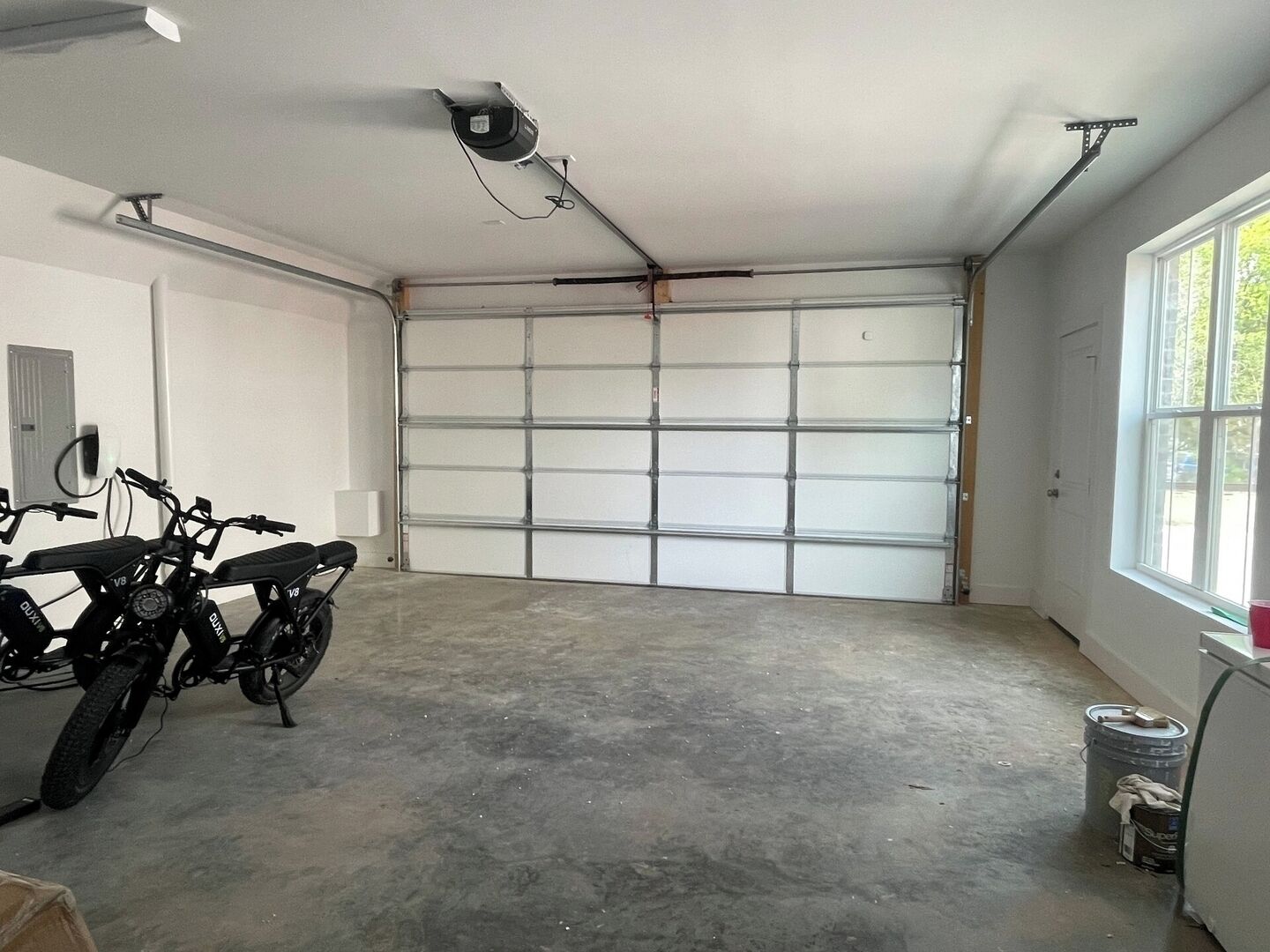 A garage with a large white garage door, two motorcycles parked inside, and a ceiling-mounted light fixture.