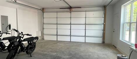 A garage with a large white garage door, two motorcycles parked inside, and a ceiling-mounted light fixture.