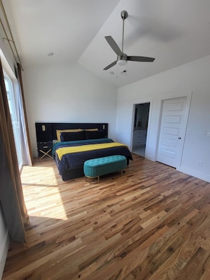 A bedroom with a bed, a bench, a ceiling fan, and wooden flooring.